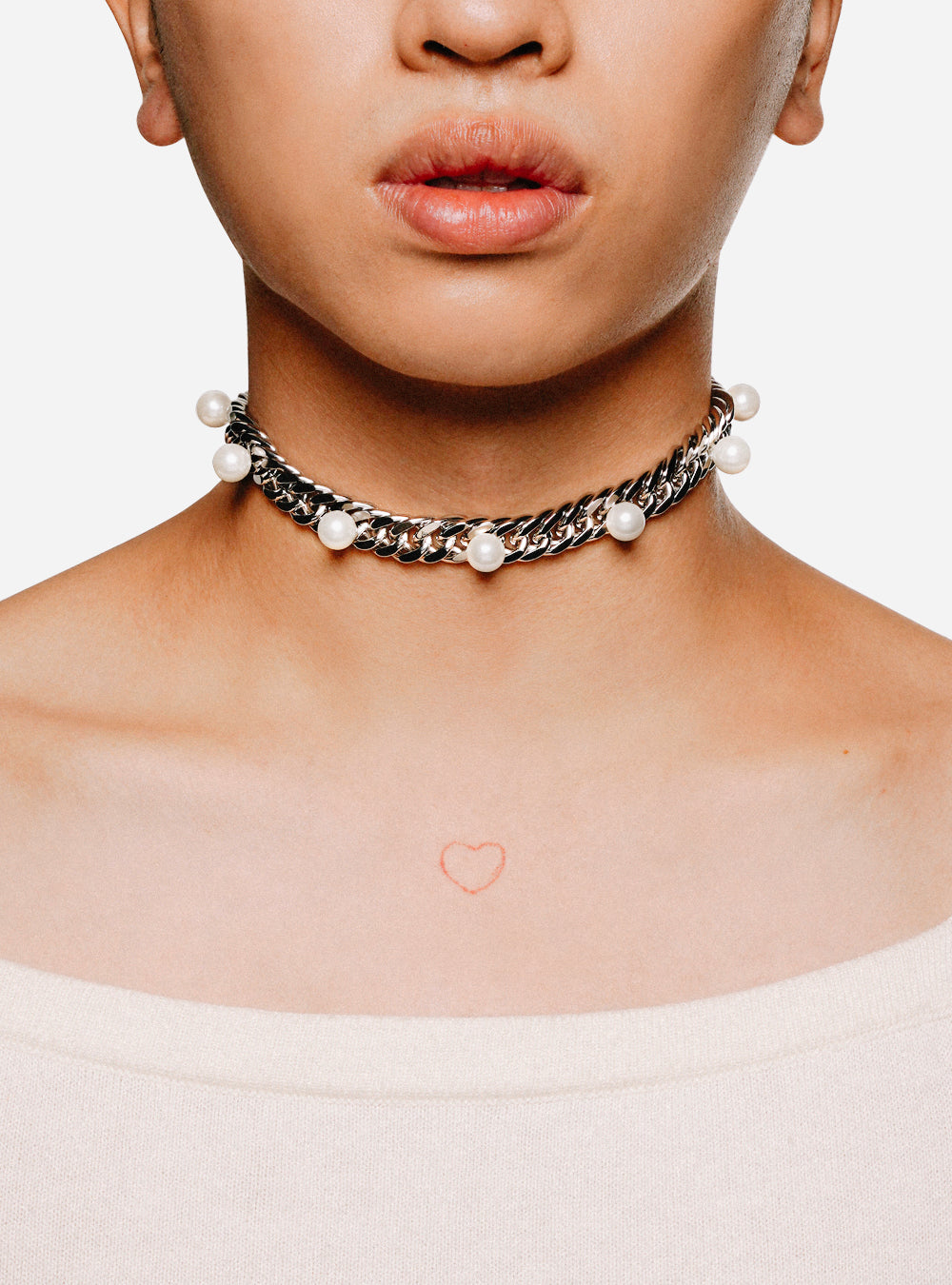 A woman wearing a "Pearls on curb-chain choker necklace" by MIDNIGHTFACTORY, with a heart on it.