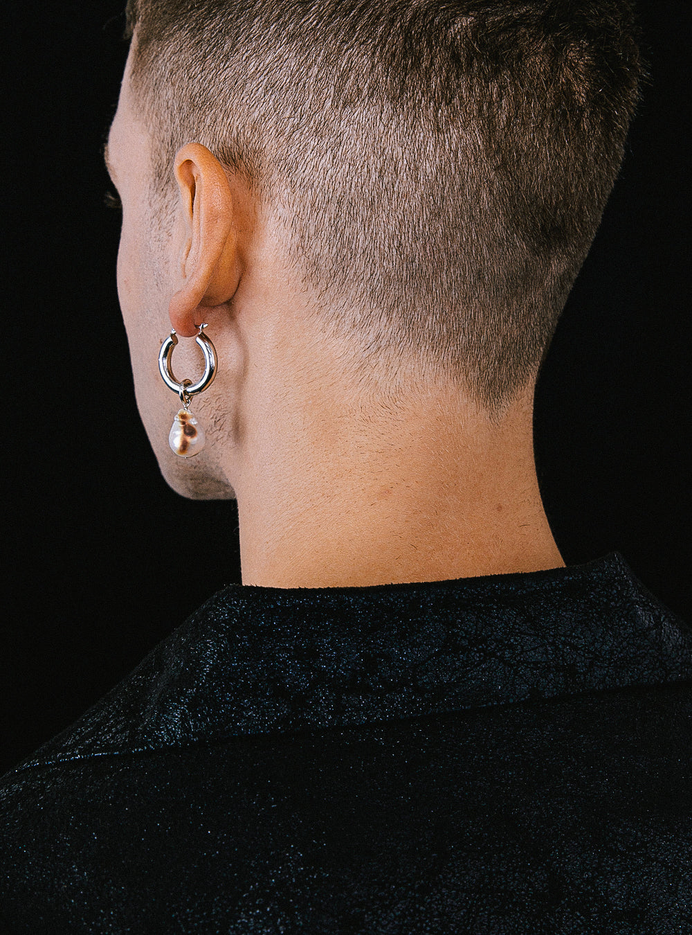 The back of a man wearing a pair of MIDNIGHTFACTORY Burnt baroque pearl earrings.