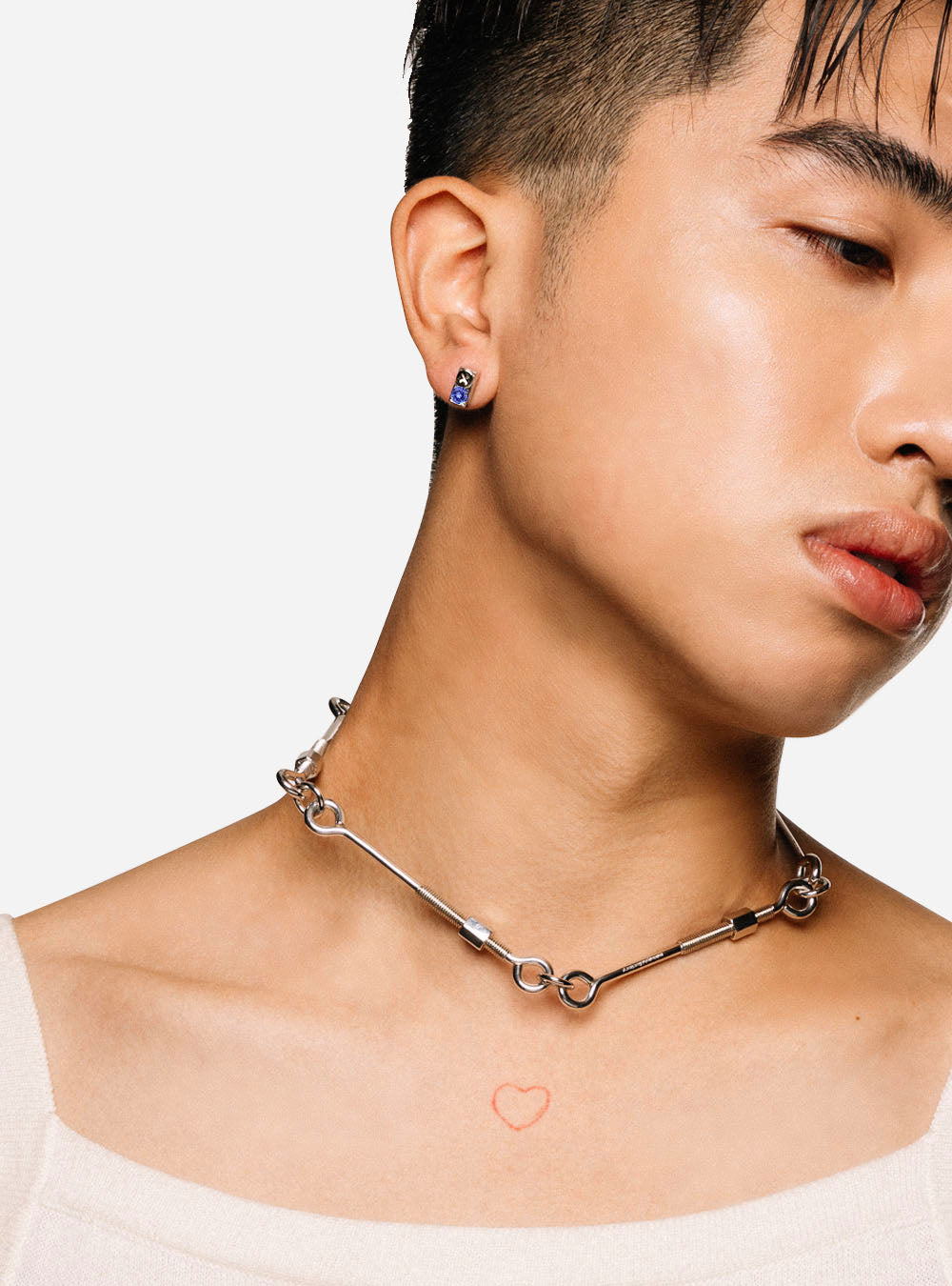 A young man wearing a MIDNIGHTFACTORY necklace with a heart on it.