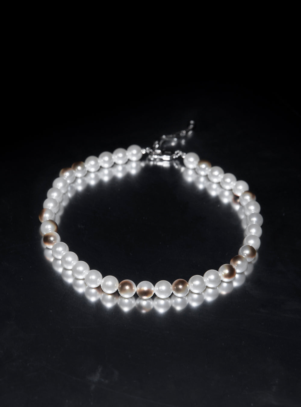 a Burnt pearls necklace by MIDNIGHTFACTORY on a black surface.