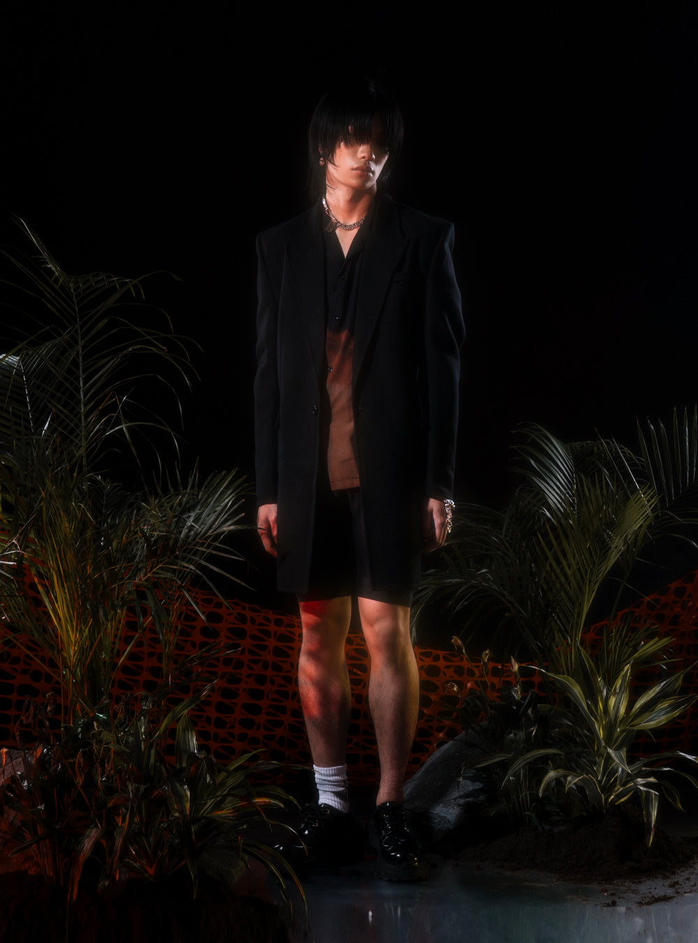 A man in a black suit standing in front of plants wearing the MidnightFactory Burnt Pearls with MNFT blade chain necklace.